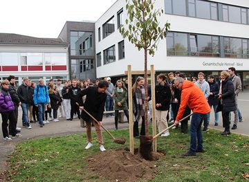 Bürgermeister Mario Dahm und Schulleiter Alfred Scholemann (rechts) helfen, den Baum einzupflanzen.
