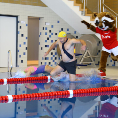 Nicht ohne meine Krawatte: Martin Herkt, Schul- und Sportdezernent der Stadt, und Kathrin Schäferling, stellvertretende Leiterin der Sportschule, weihen das sanierte Schwimmbecken ein, nachdem Sportschul-Maskottchen Henni ihnen ein kräftigen Schubs gegeben hat